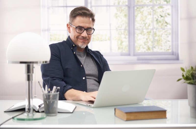 An options trader smiles while looking at his laptop computer screen.